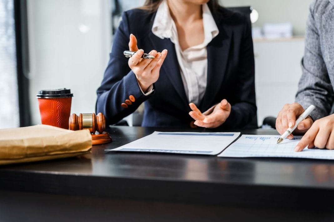 Two female lawyers in business suits meet at wooden desk, shaking hands over contract paper. wooden gavel and scales justice as discuss legal compliance, corporate law, dispute resolution. avocat en droit du commerce